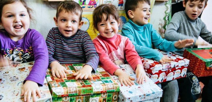 Kinder mit Geschenken von "Weihnachten im Schuhkarton" auf dem Schoß